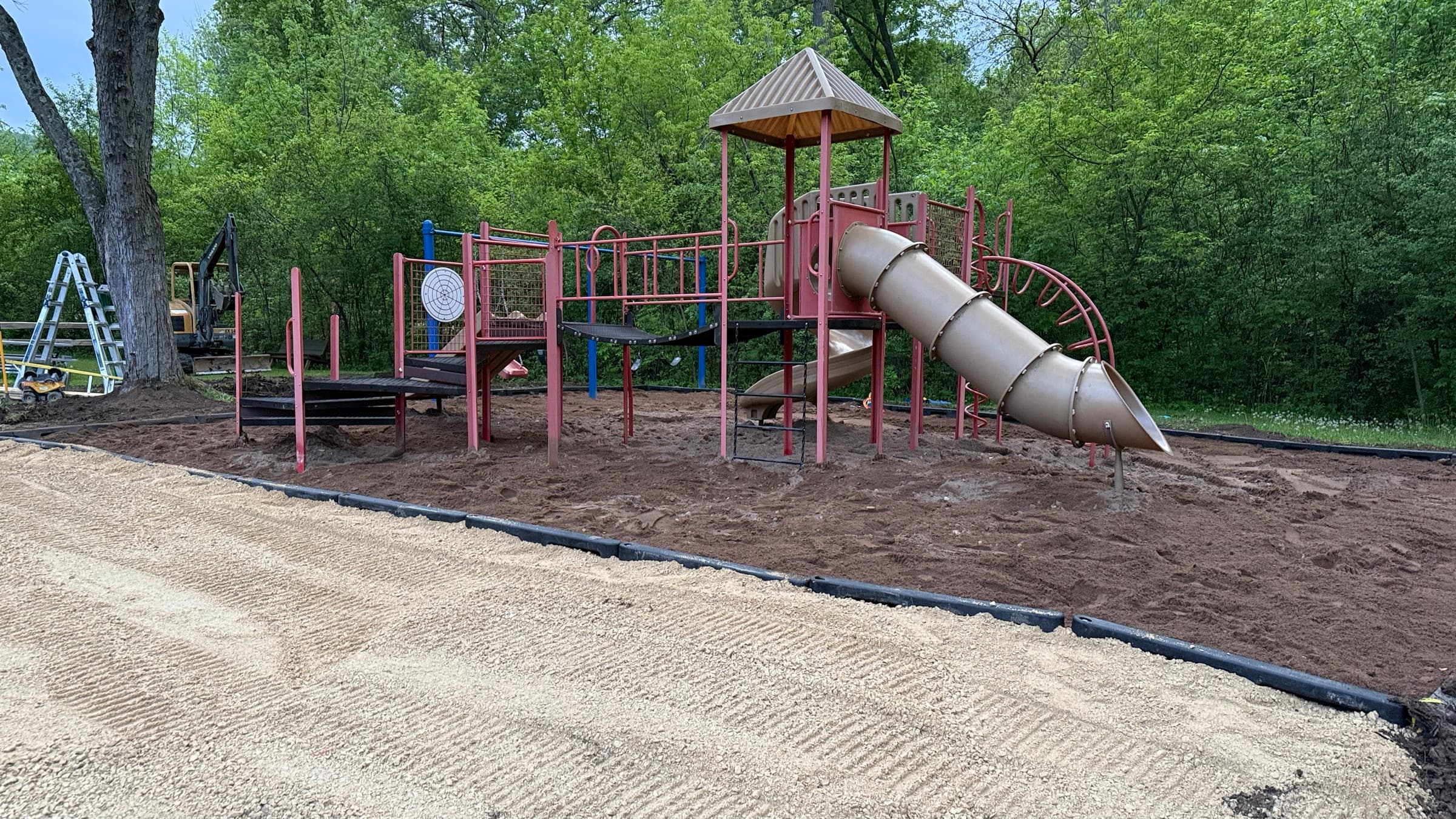 Large playground structure at Camp Everyday Winona with a climbing tower, tube slide, and soft sand base, surrounded by trees along the Mississippi River bluffs